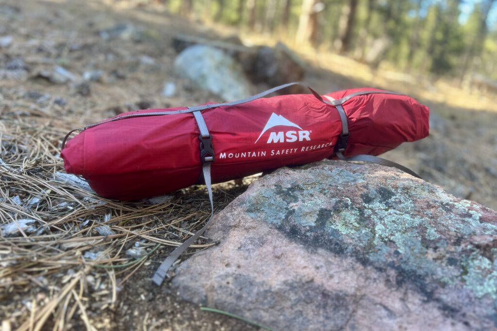 a red msr tent sits packed up on a rock