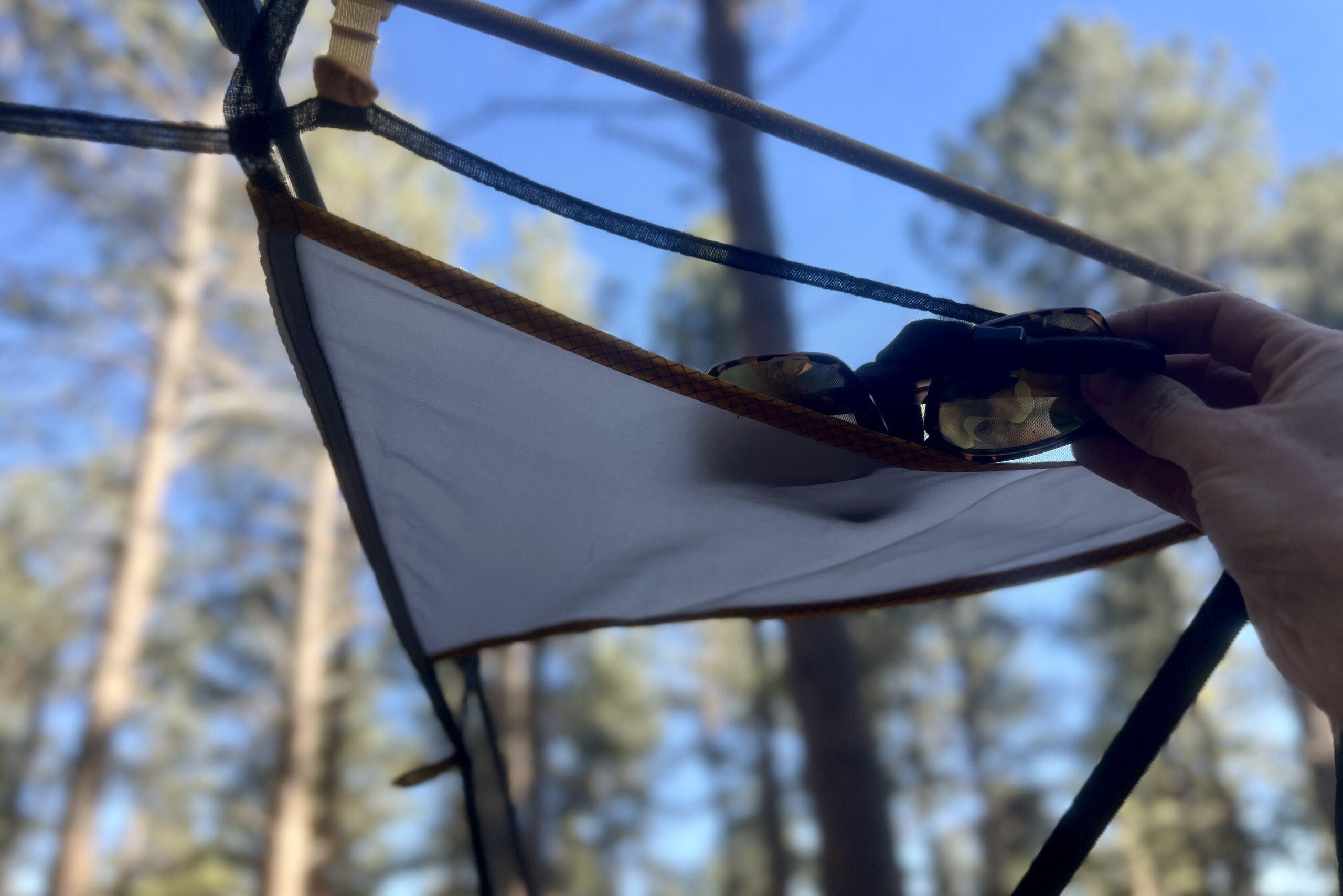 a hand stuffs a pair of sunglasses into a tent's interior ceiling pocket