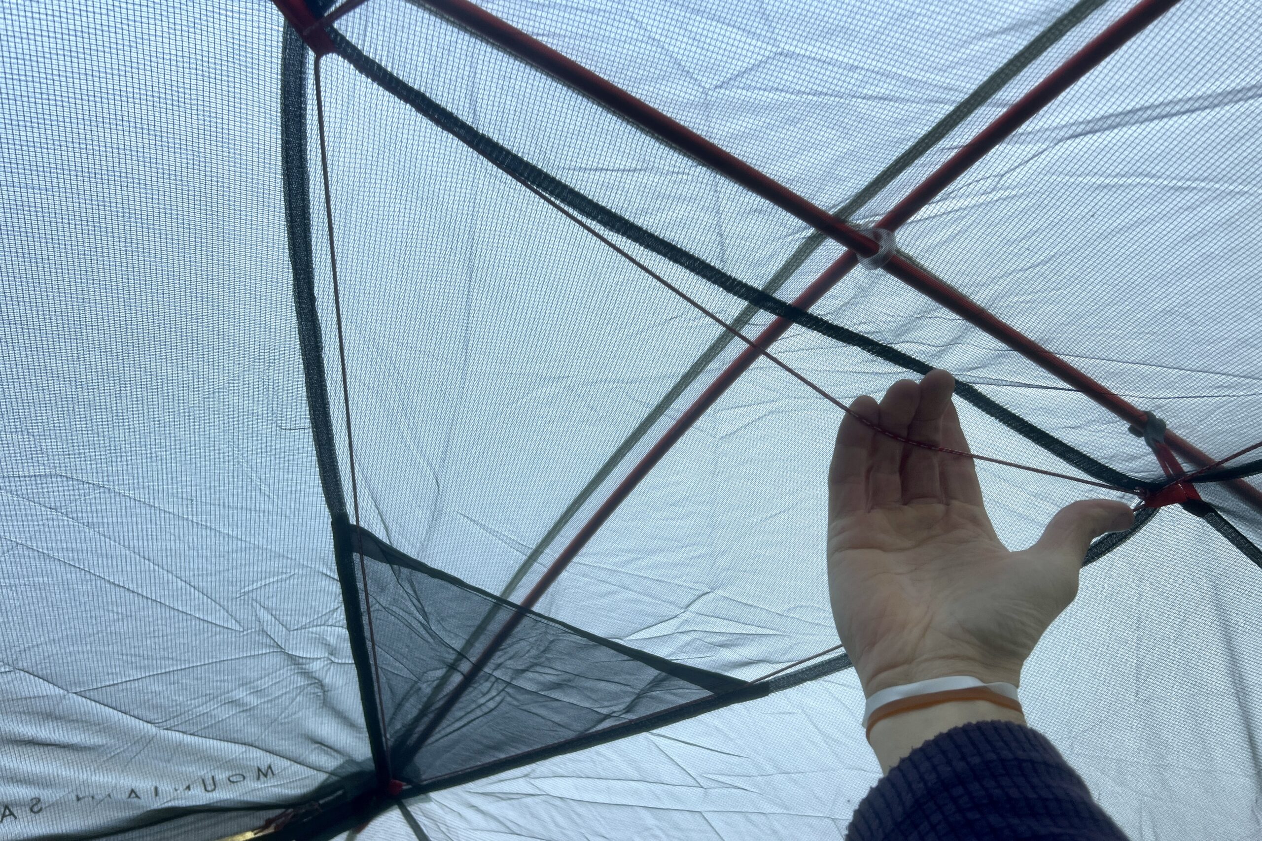 a hand reaches up to pull on a cord that is stretch across the ceiling of a tent.
