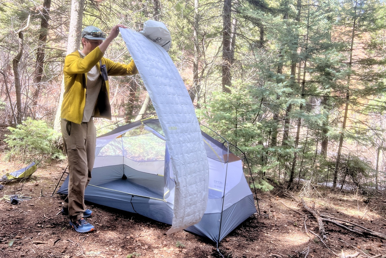 a hiker tosses a deflated gray sleeping pad next to a tent
