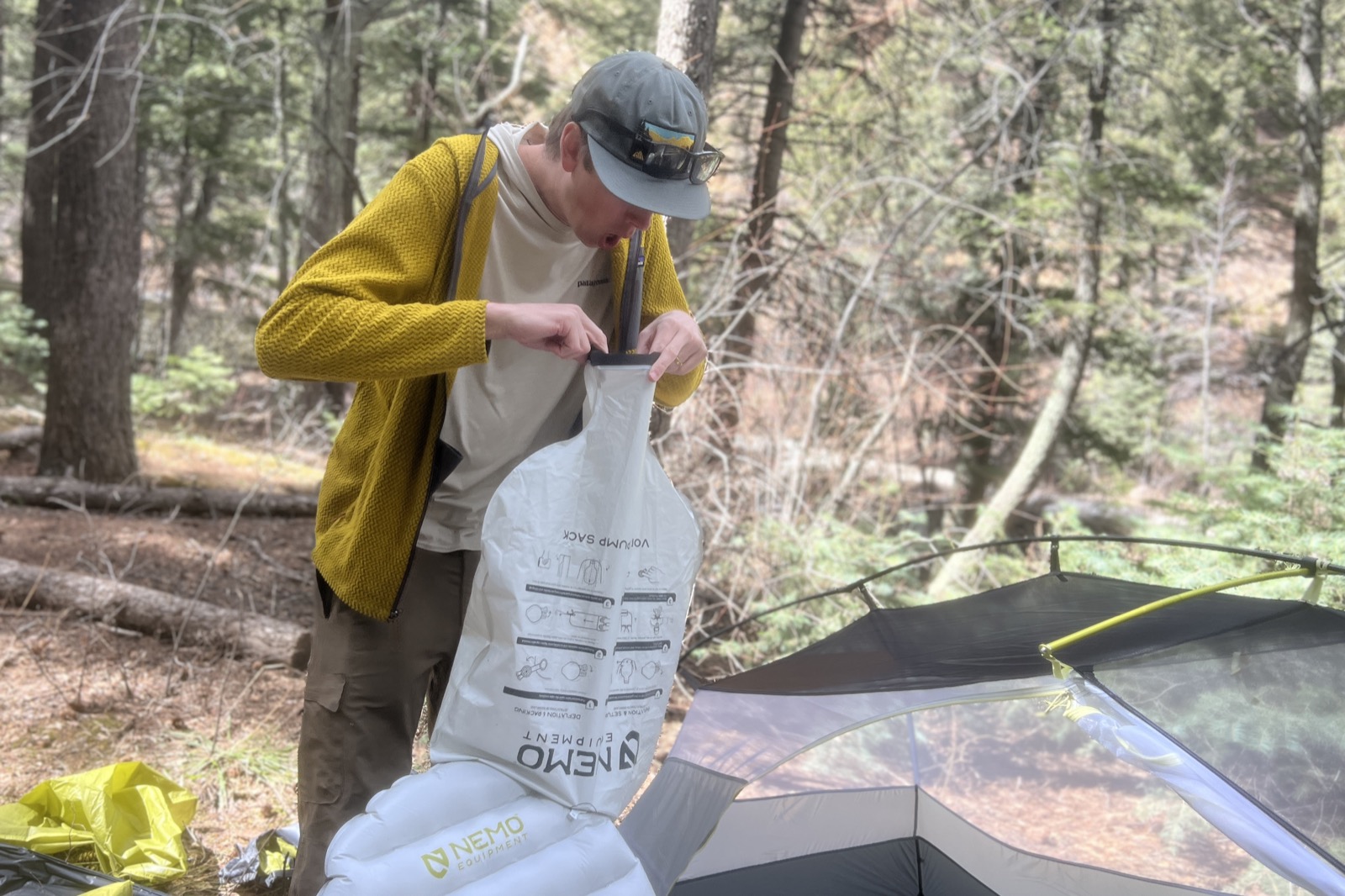 a hiker blows into a pump sack attached to a gray sleeping pad