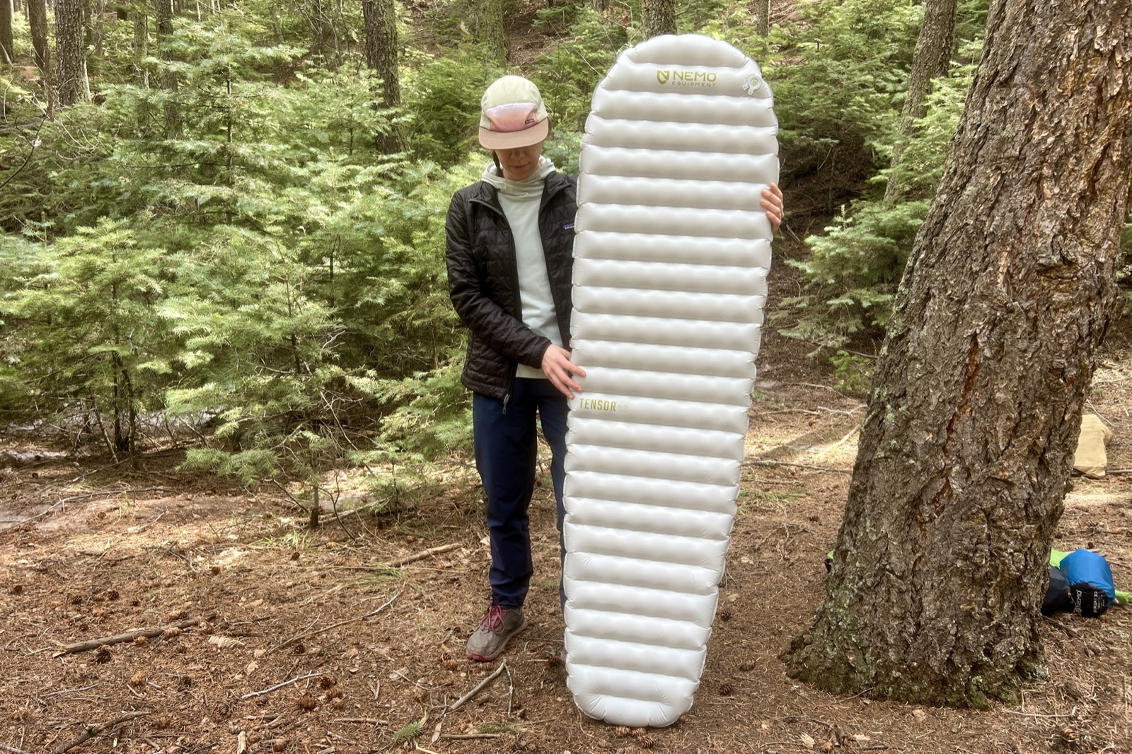 a hiker stands in the woods and holds up a gray sleeping pad.