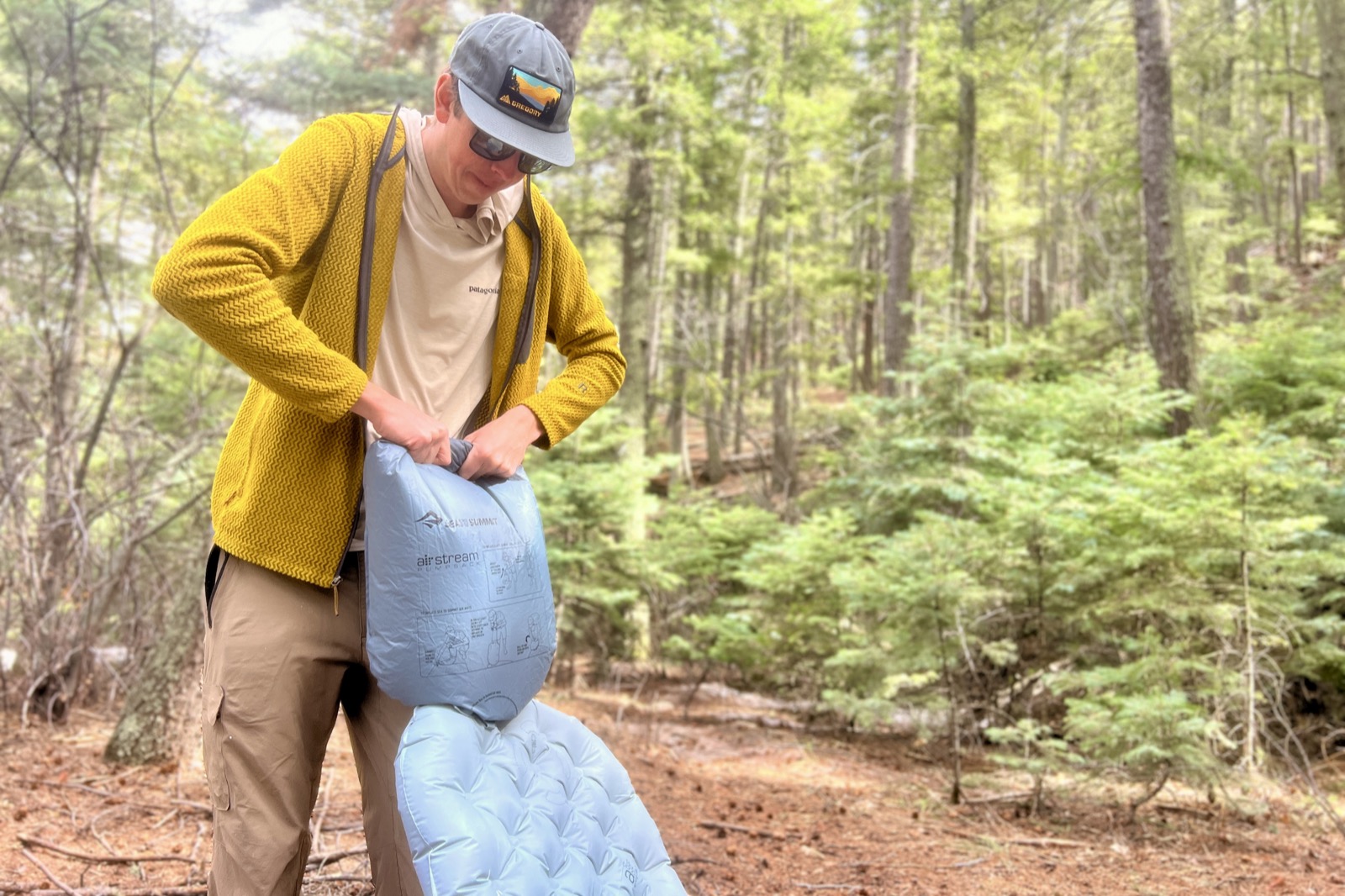 a hiker uses a pump sack to inflate a gray sleeping pad