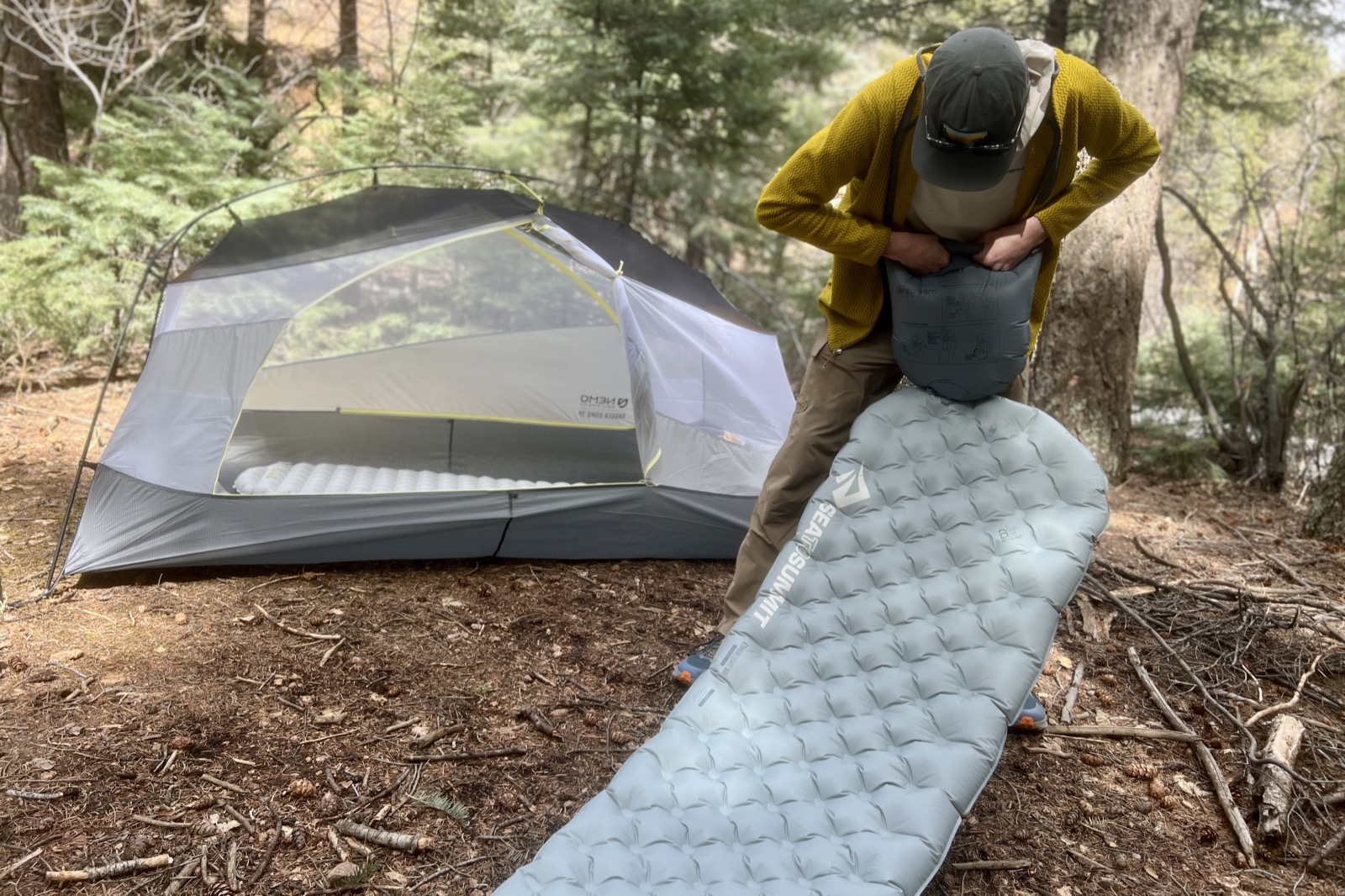 a hiker uses a pump sack to inflate a gray sleeping pad