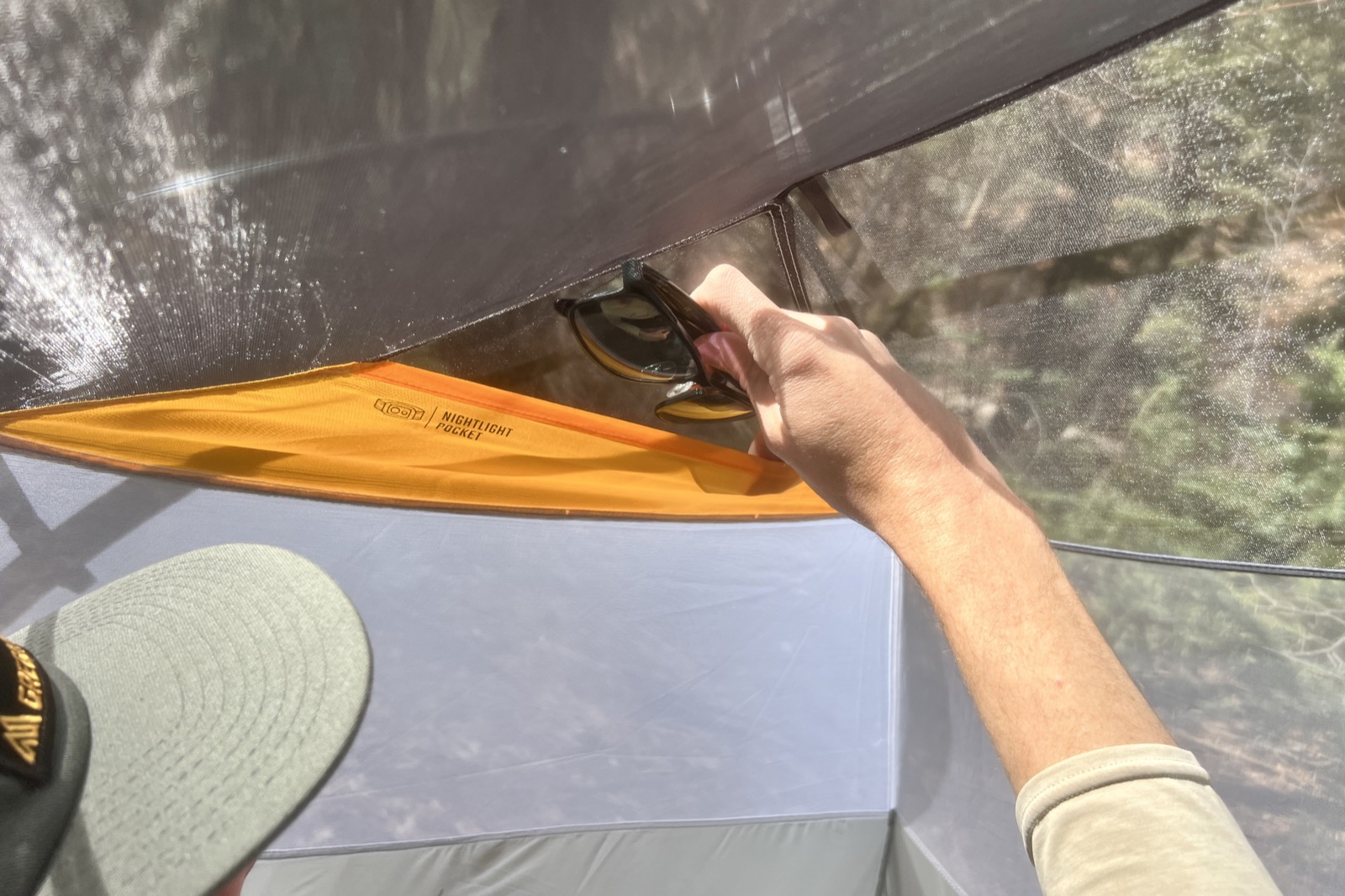 a hiker stuffs a pair of sunglasses into a mesh pocket of a tent