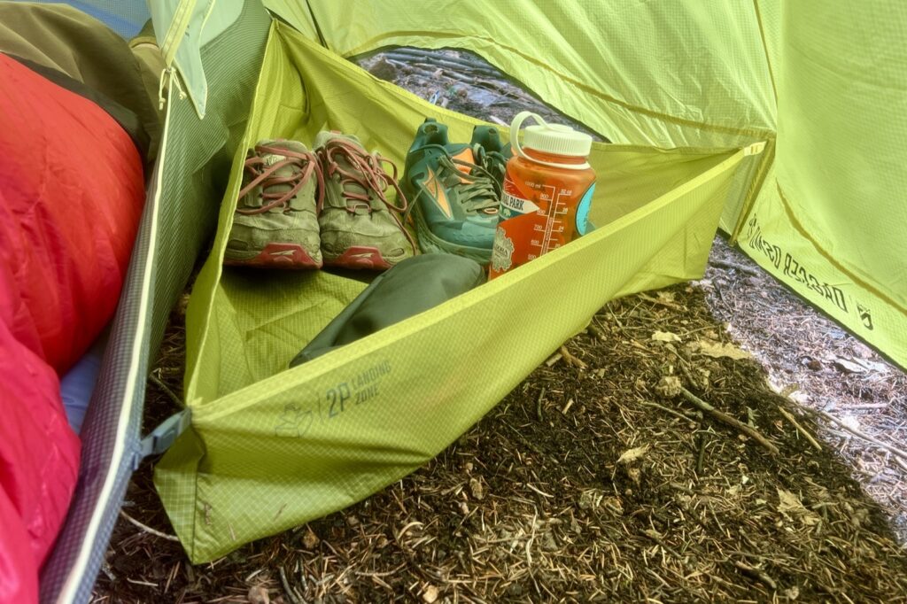 shoes and a water bottle resting in the gear landing zone in a tent's vestibule.