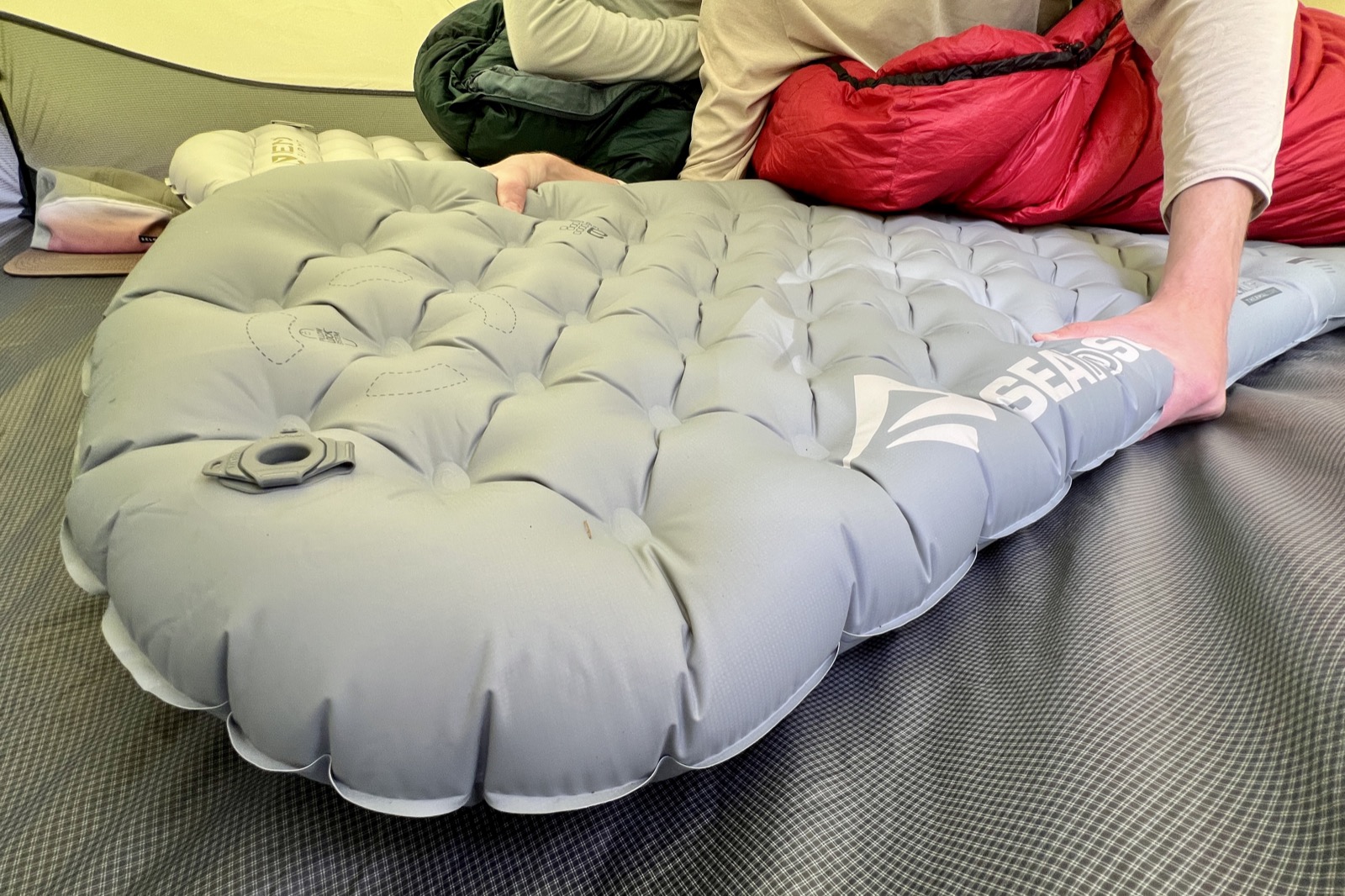 a hiker grasps a gray sleeping pad in a tent