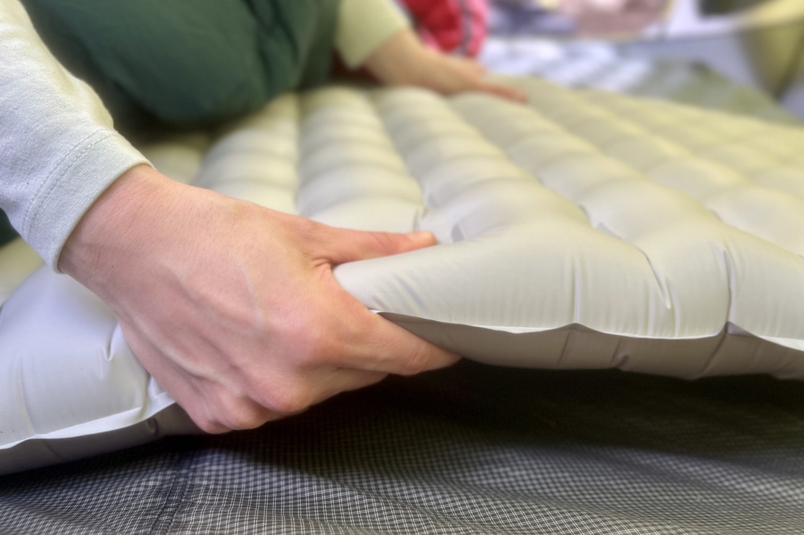 a close up of a hiker grasping the thickness of a gray sleeping pad