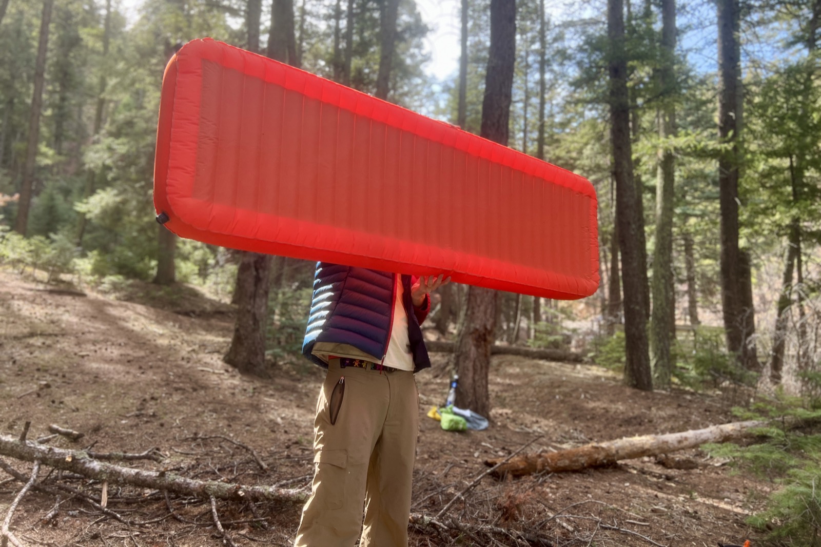 A hiker holds a red sleeping pad in the air in the middle of the woods