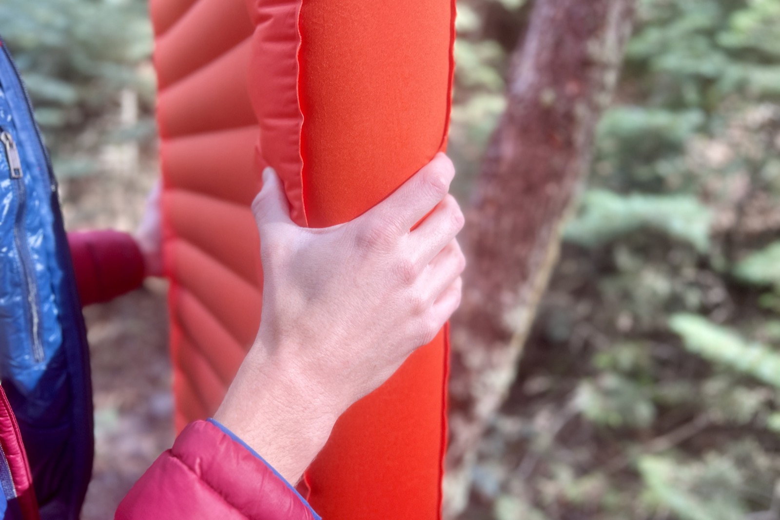 a closeup of a hand grasping the thickness of a sleeping pad