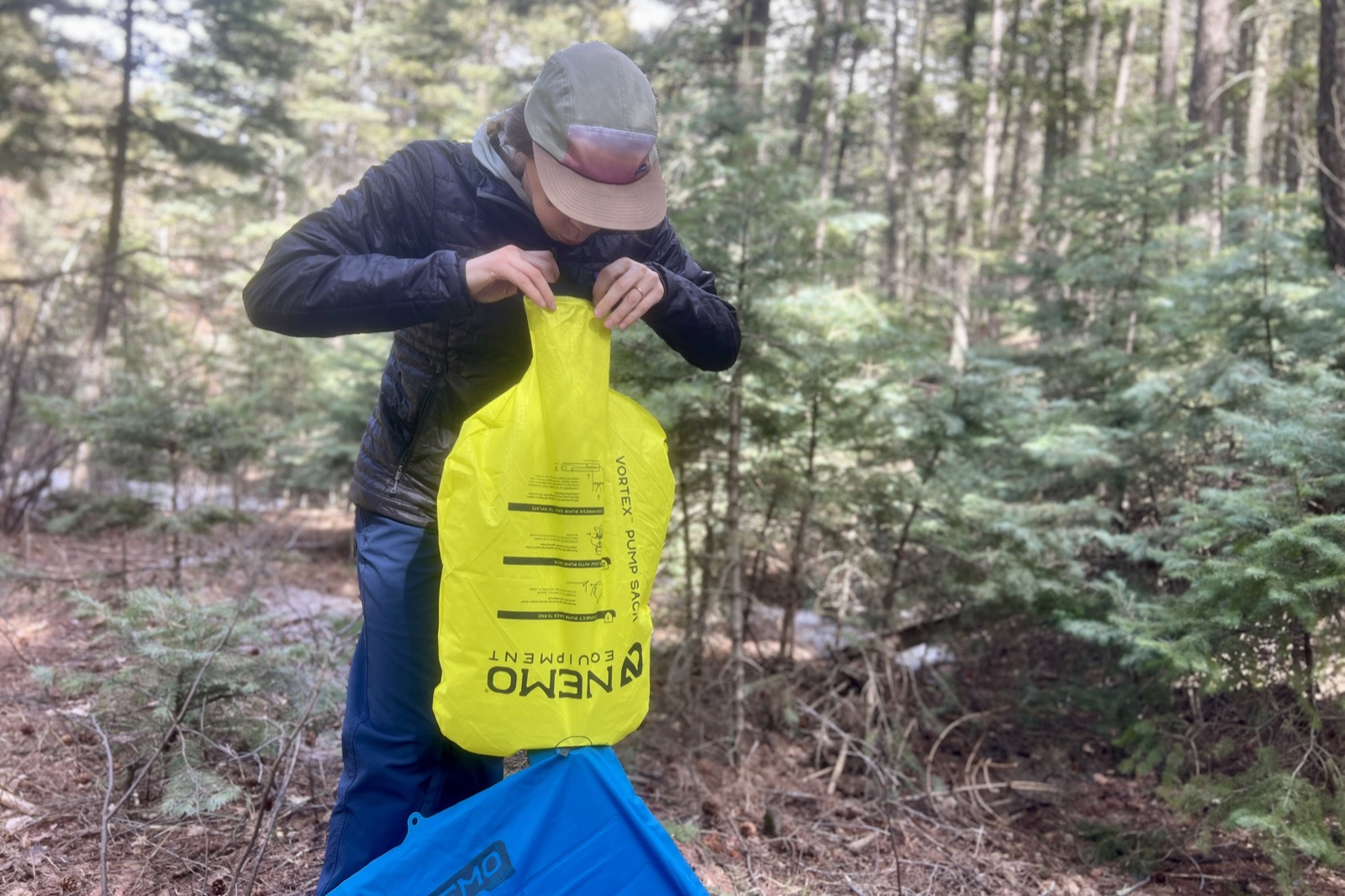 a hiker blows into a pump sack attached to a blue sleeping pad