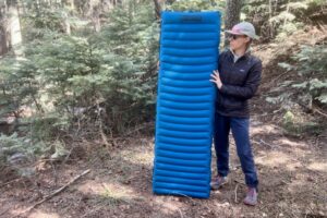 a hiker stands in the woods and holds up a blue sleeping pad.
