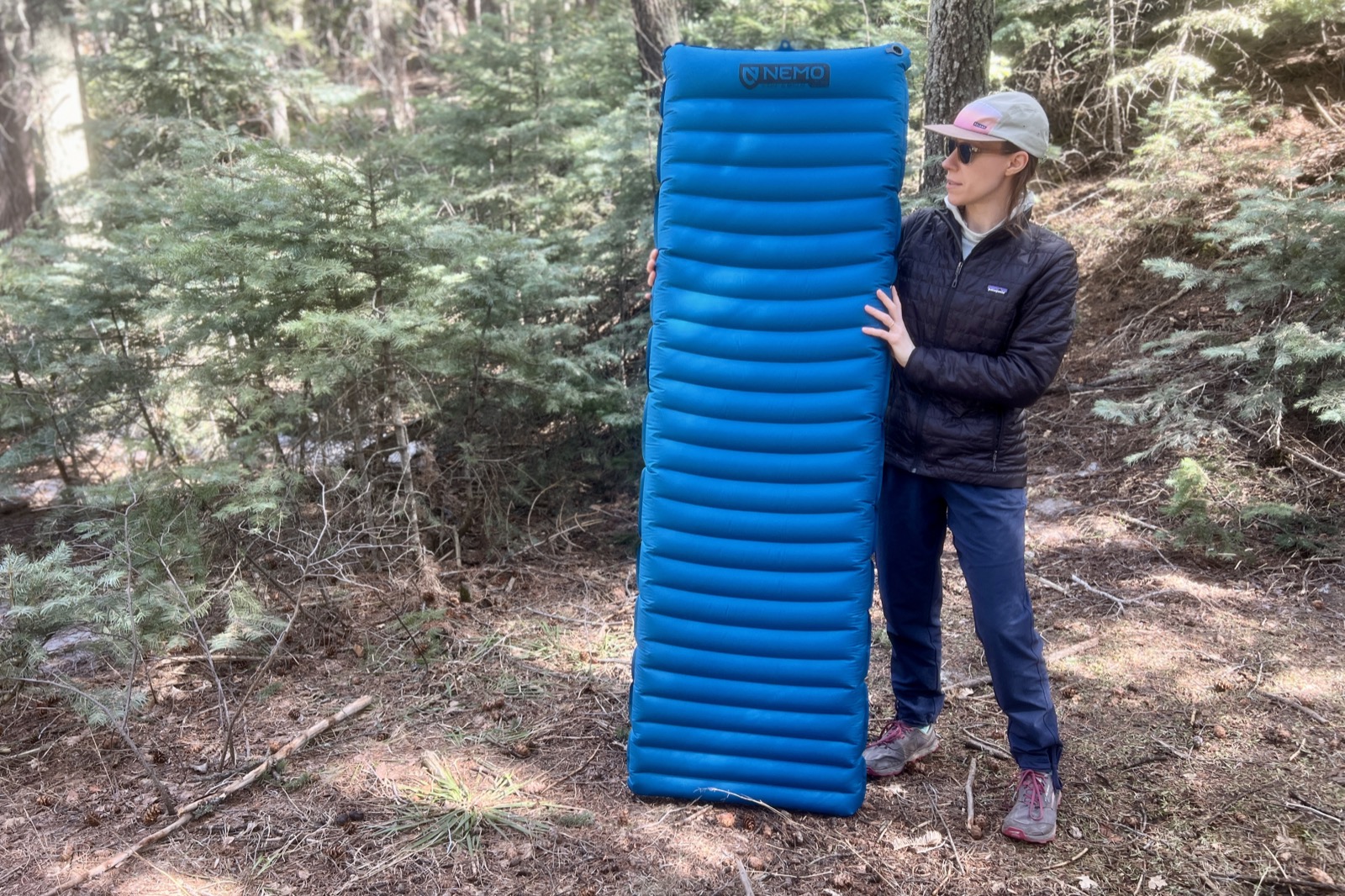 a hiker stands in the woods and holds up a blue sleeping pad.