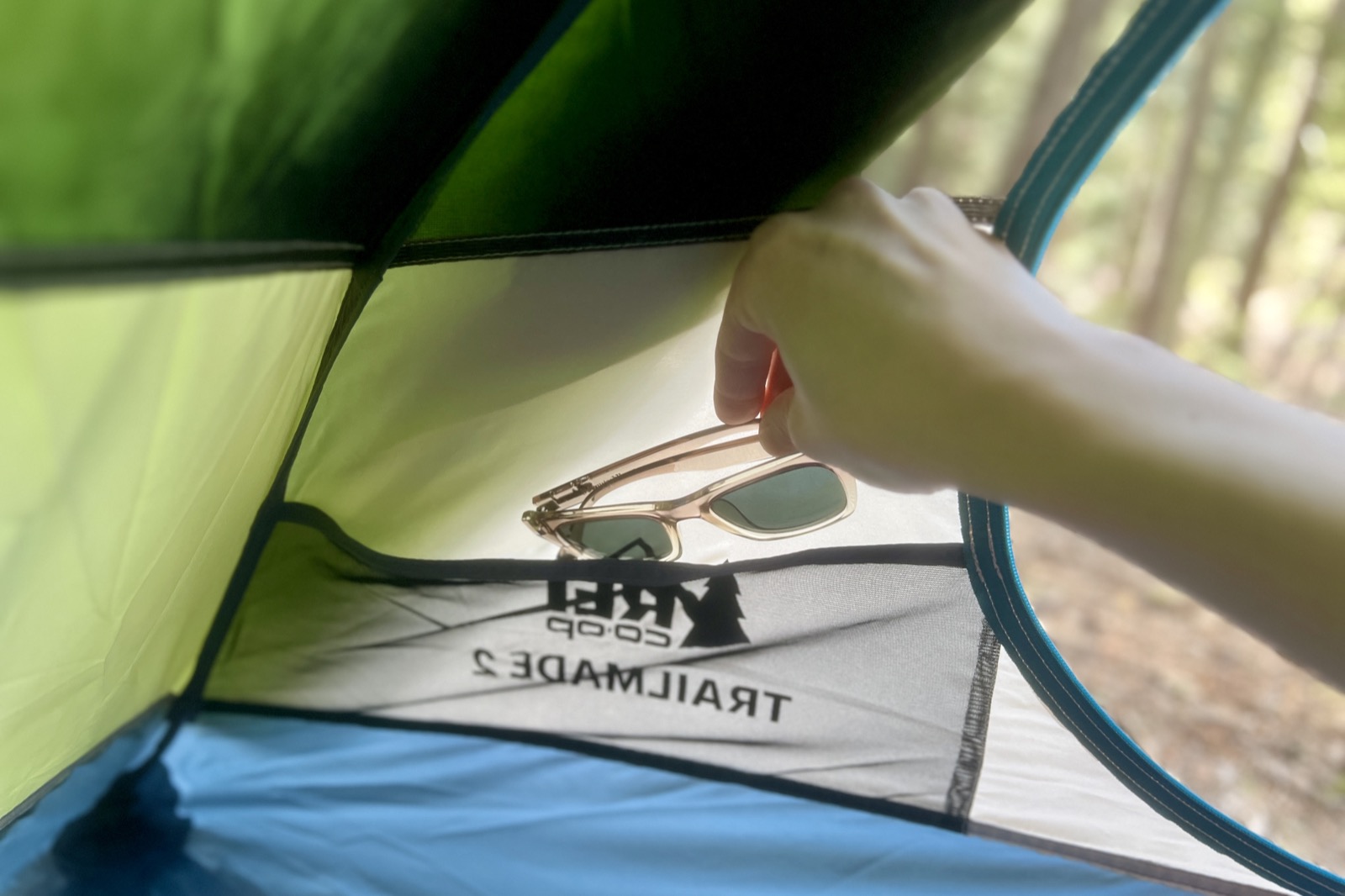 a hand stuffs a pair of sunglasses into a mesh pocket in a tent