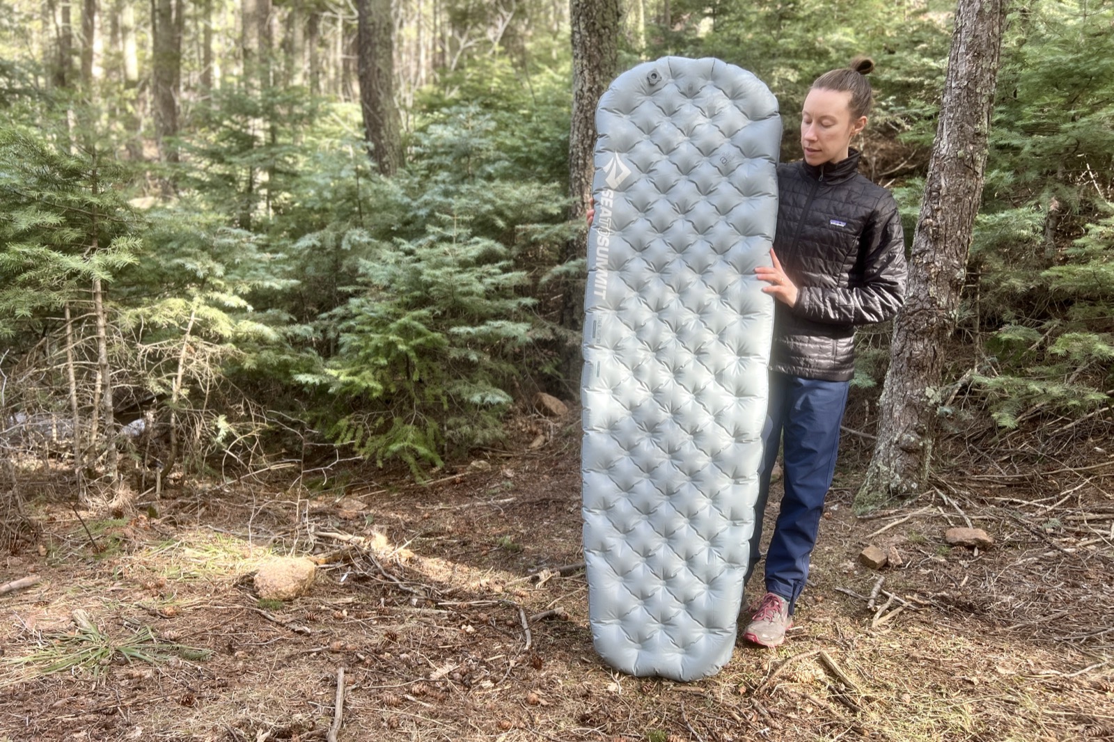 a hiker stands in the woods and holds up a gray sleeping pad.