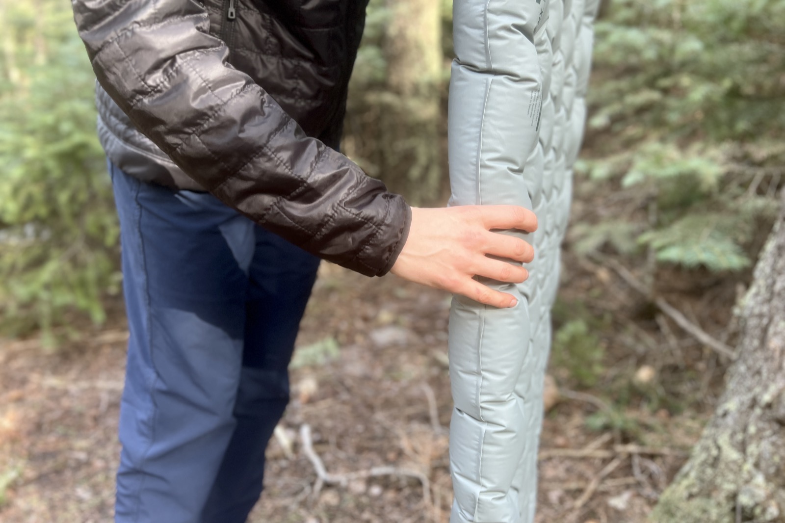 a close up of a hiker grasping the thickness of a blue sleeping pad