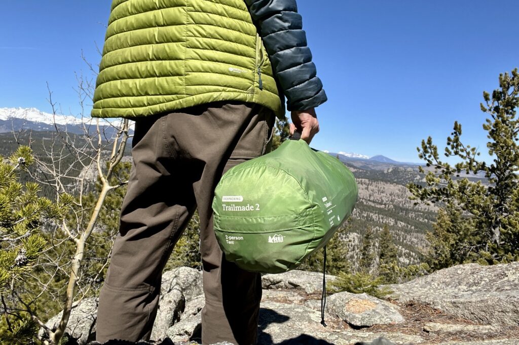 a hiker holds a green tent packed in its stuff sack