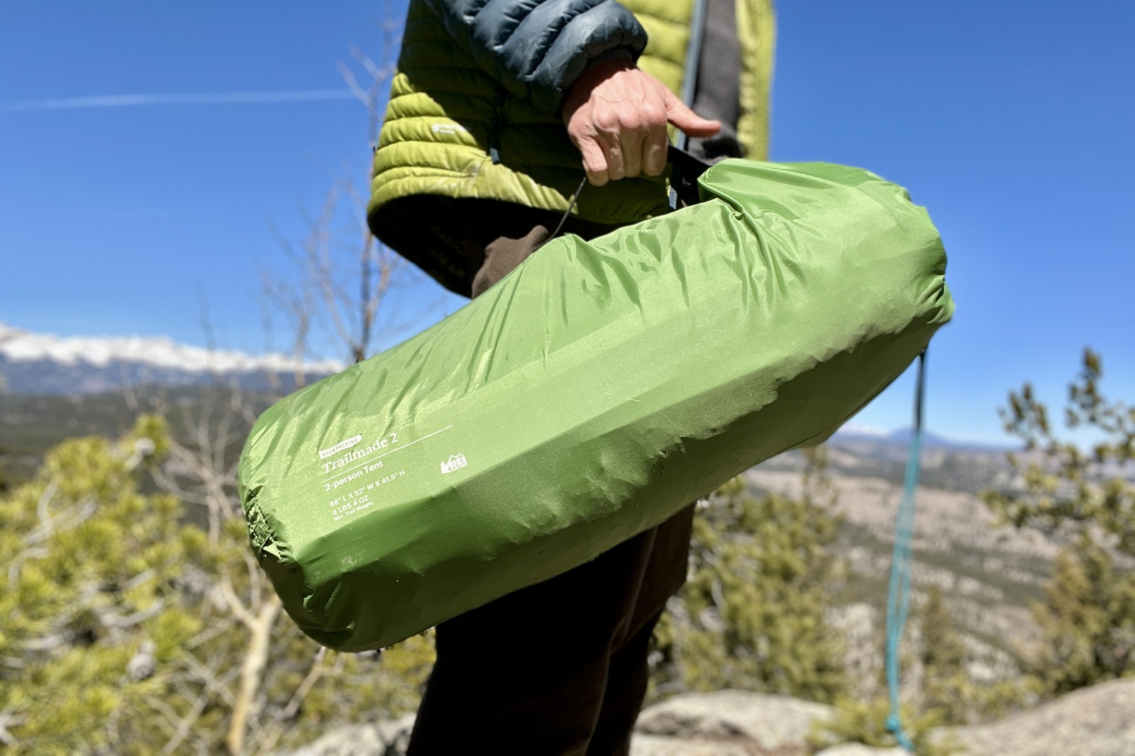 a hiker holds a green tent packed in its stuff sack