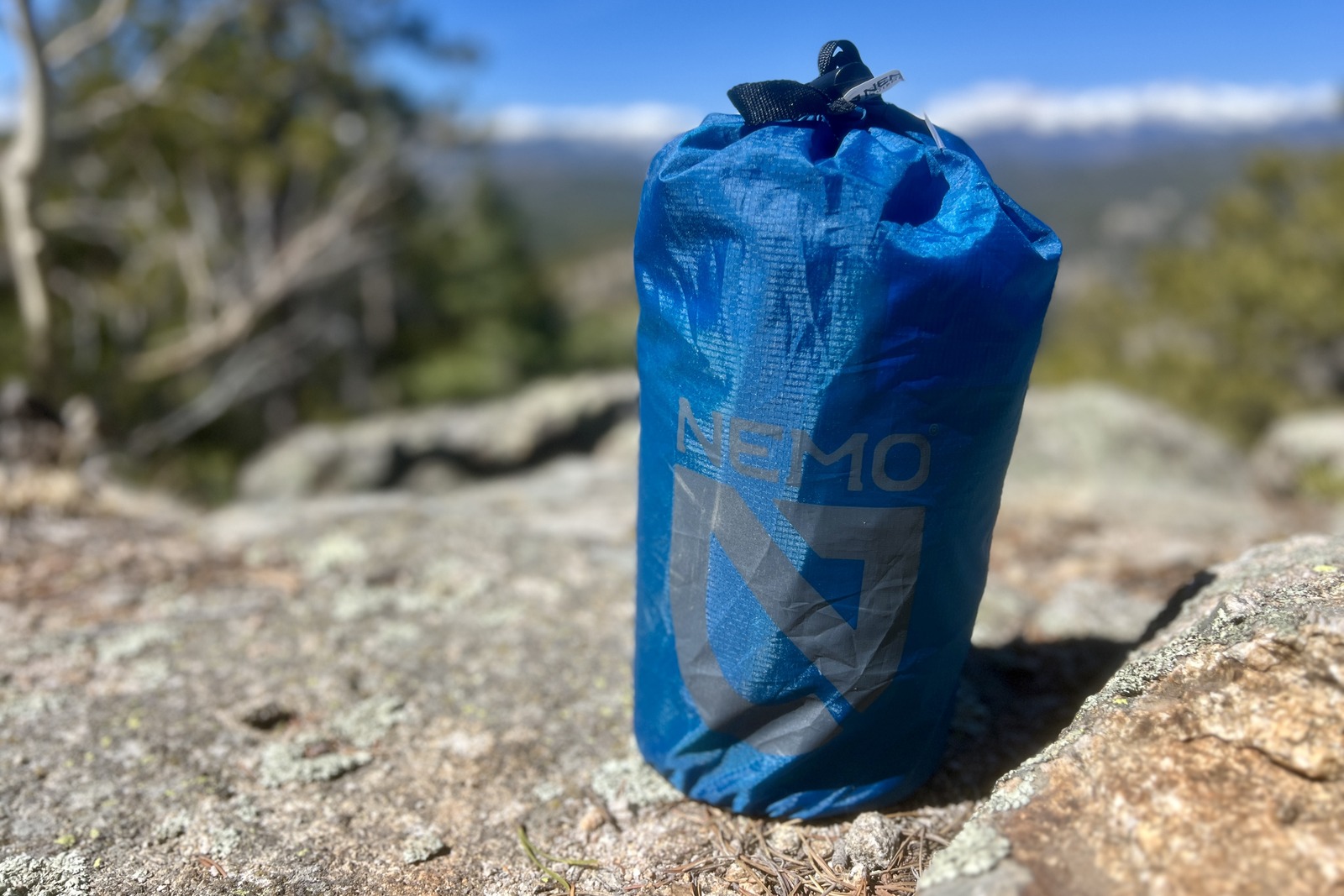 a blue stuff sack containing a sleeping pad sits on a rock