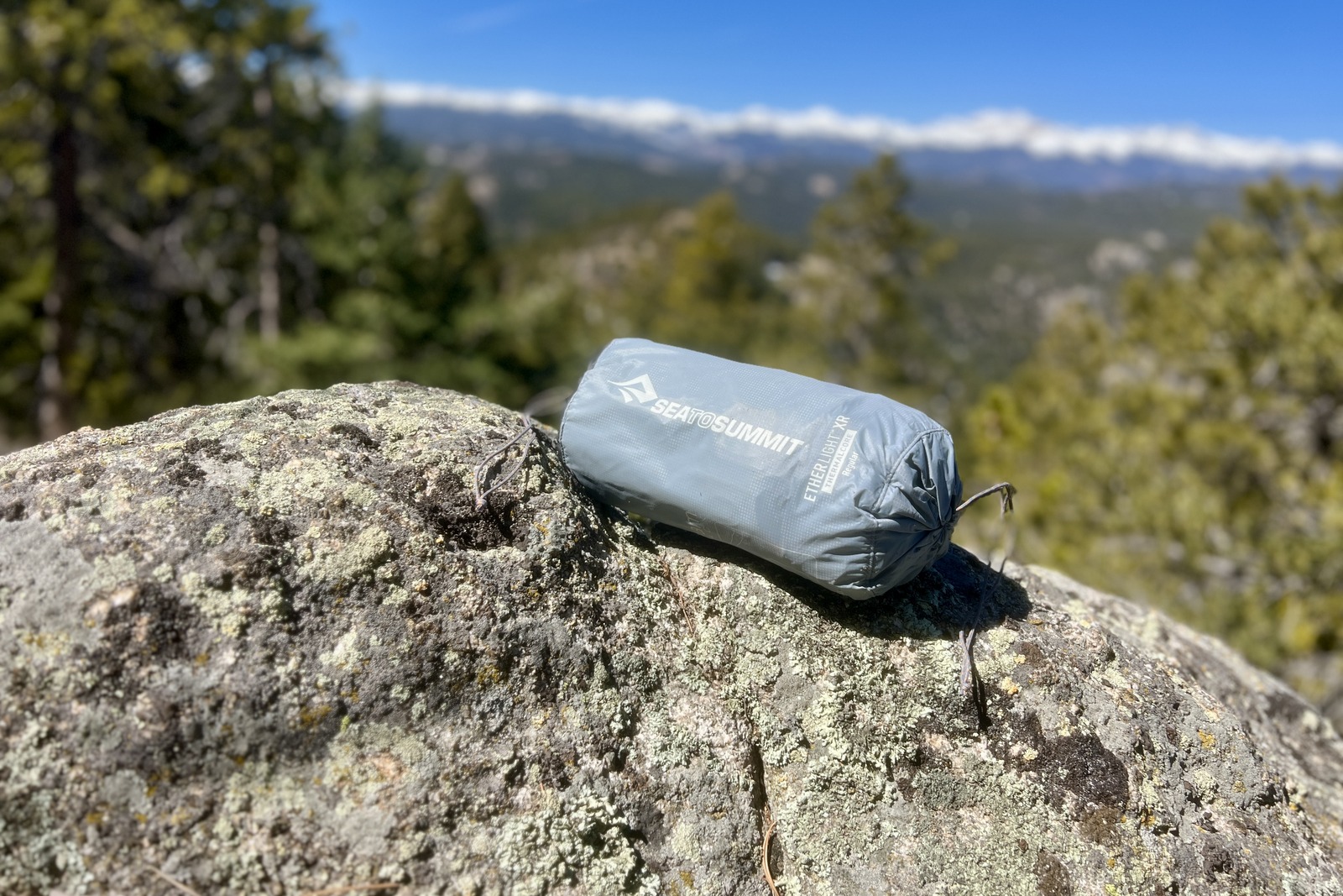 a grey stuff sack containing a sleeping pad sits on a rock
