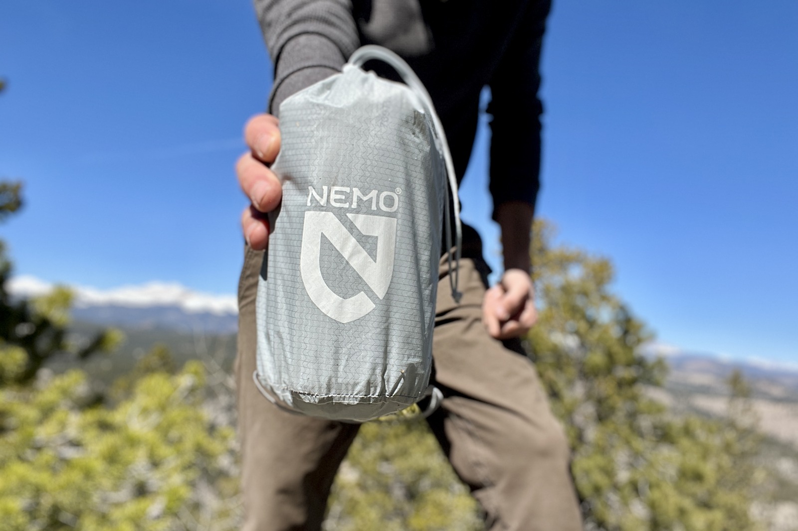 a hiker holds a gray stuff sack containing a sleeping pad