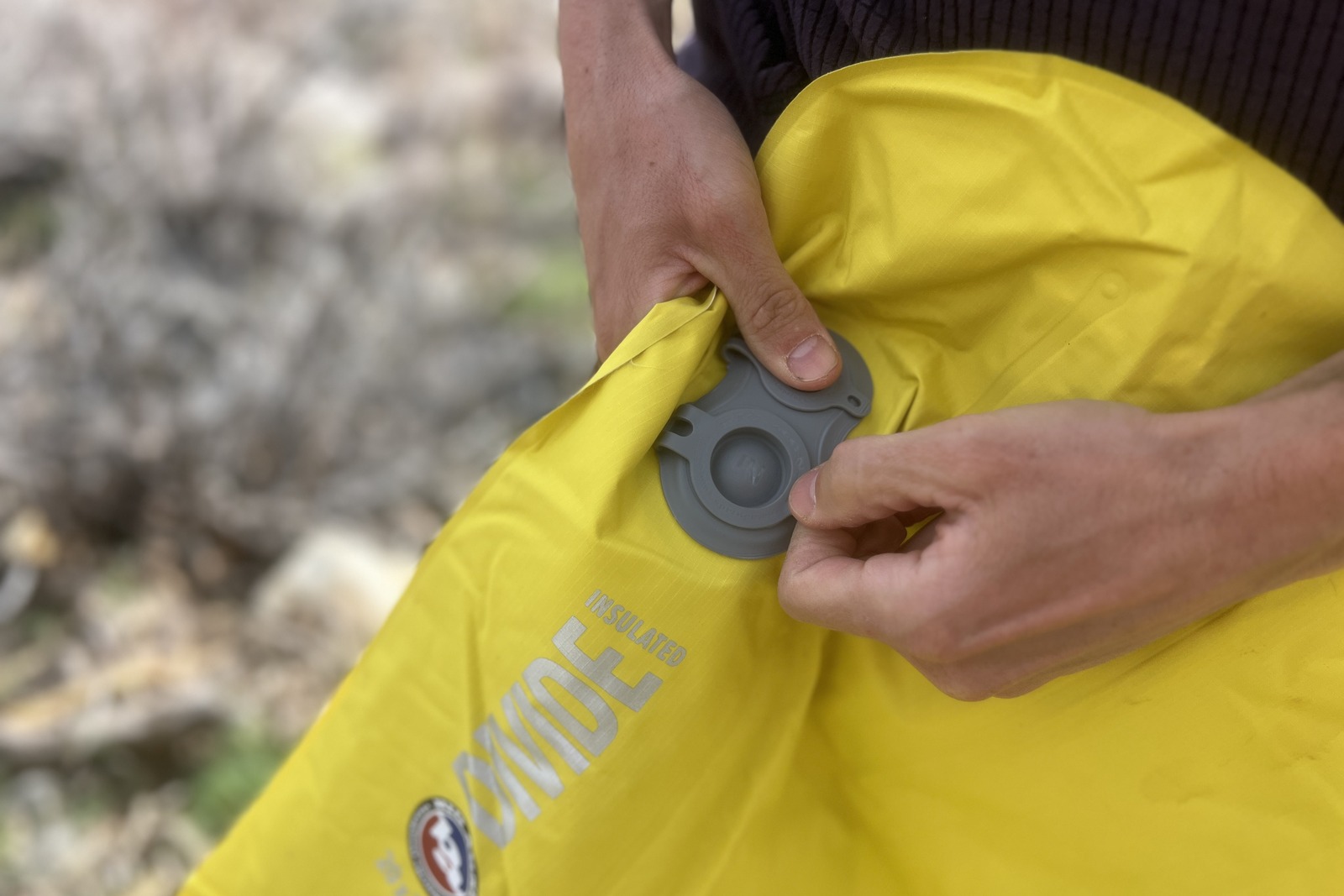 a closeup of a hiker opening the air valve on a sleeping pad