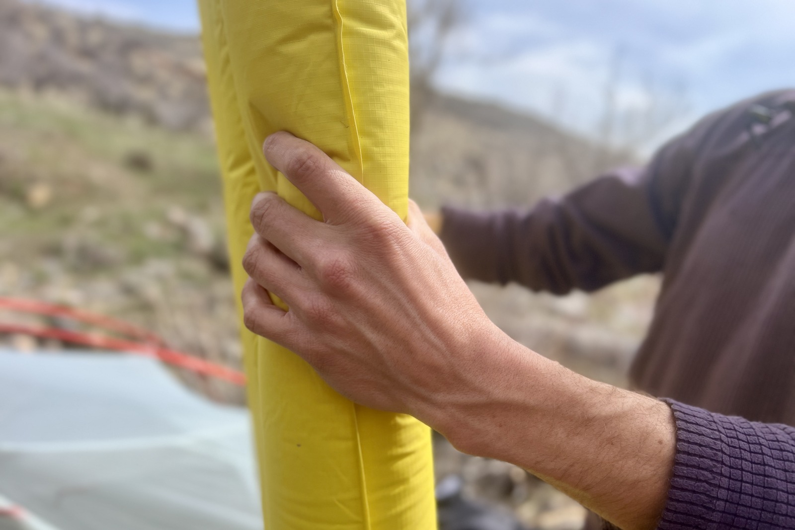 a close up of a hiker grasping the thickness of a blue sleeping pad