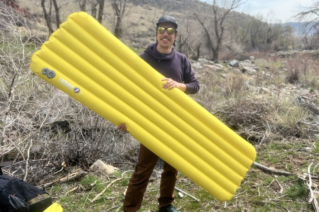 a hiker holds a yellow sleeping pad in a forest