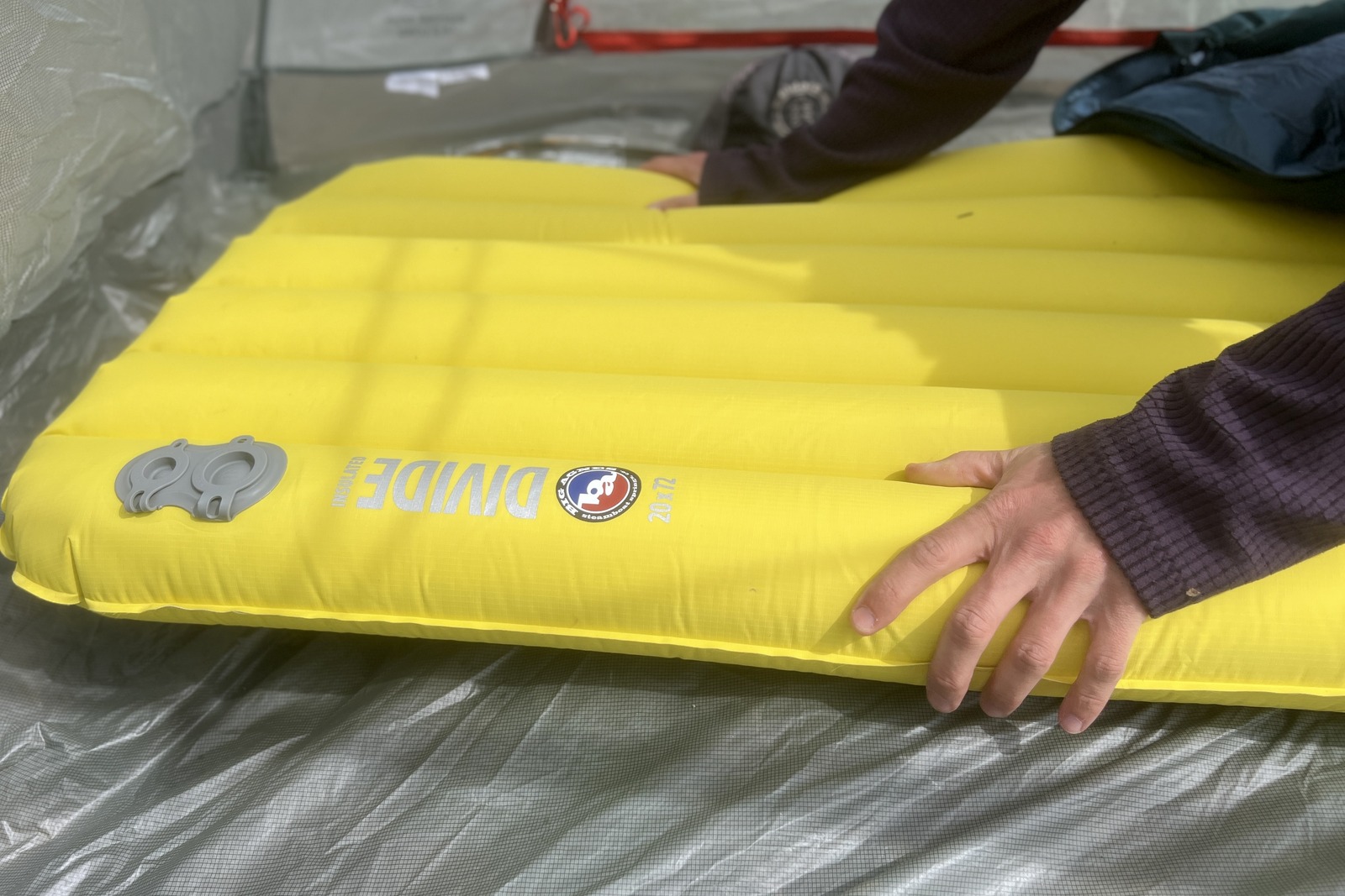 a hiker grasps a yellow sleeping pad in a tent
