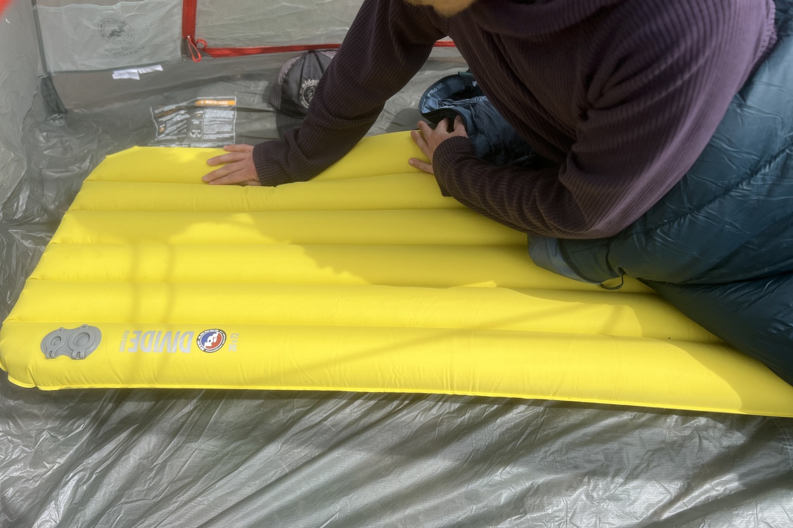 a hiker sits up on a yellow sleeping pad in a tent