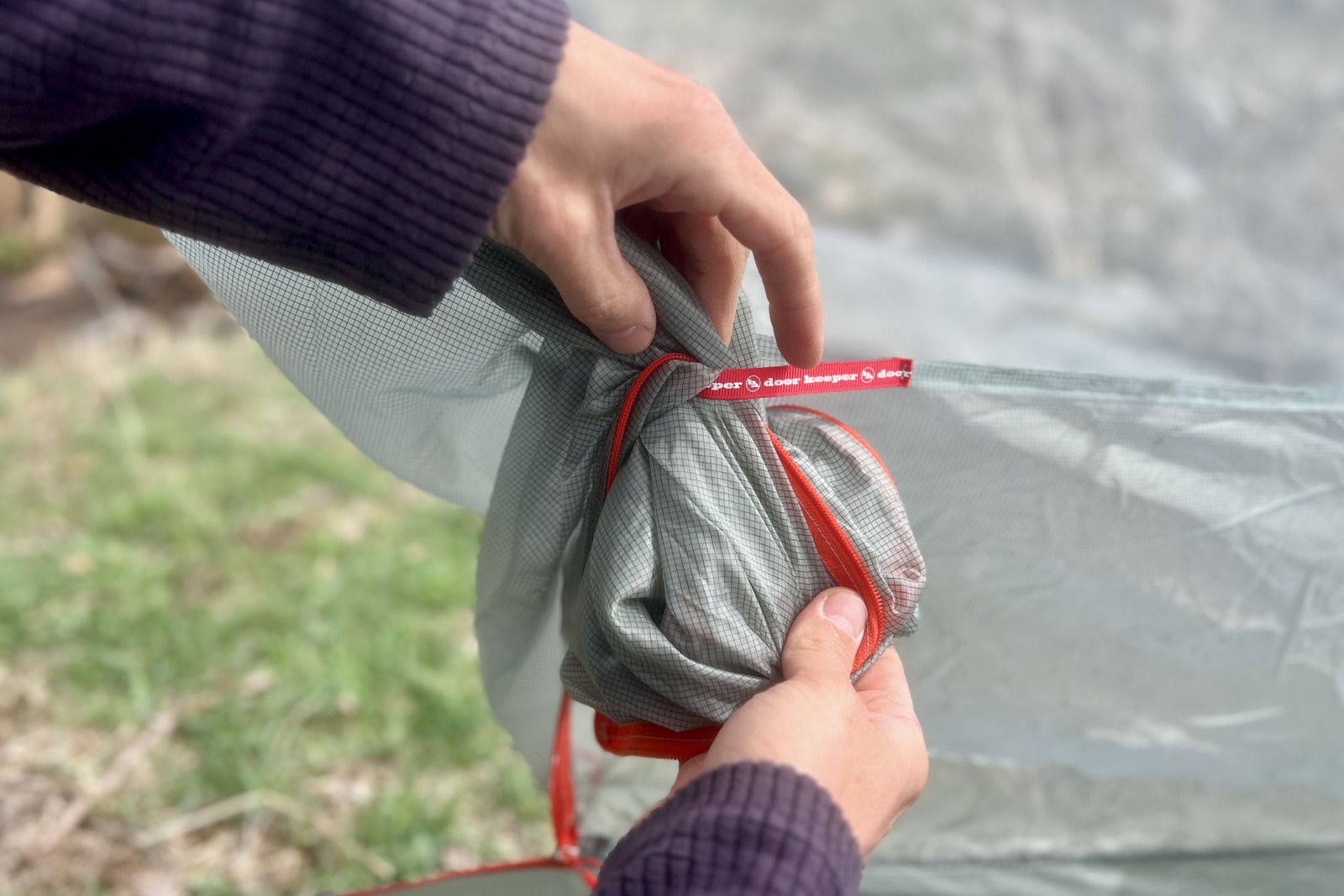 a close up of a hiker stuffing the door of a tent into its door keeper