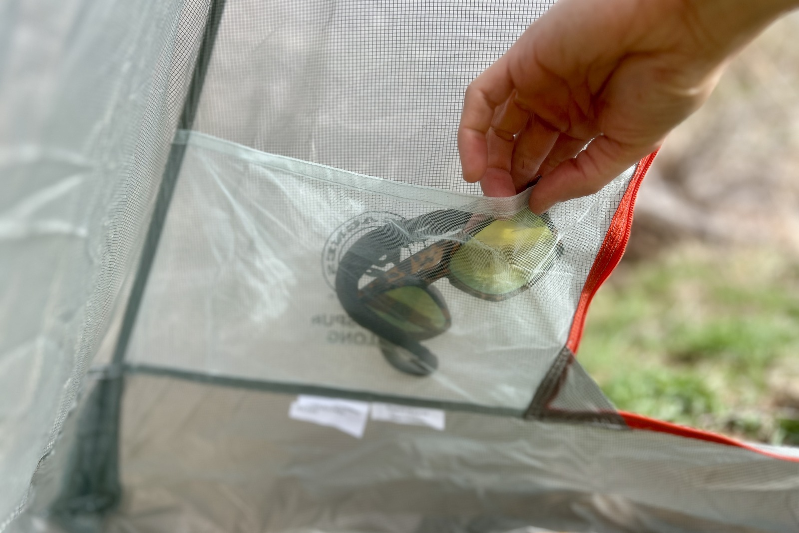 aa close up of a hiker stuffing a pair of sunglasses into the mesh pocket of a tent