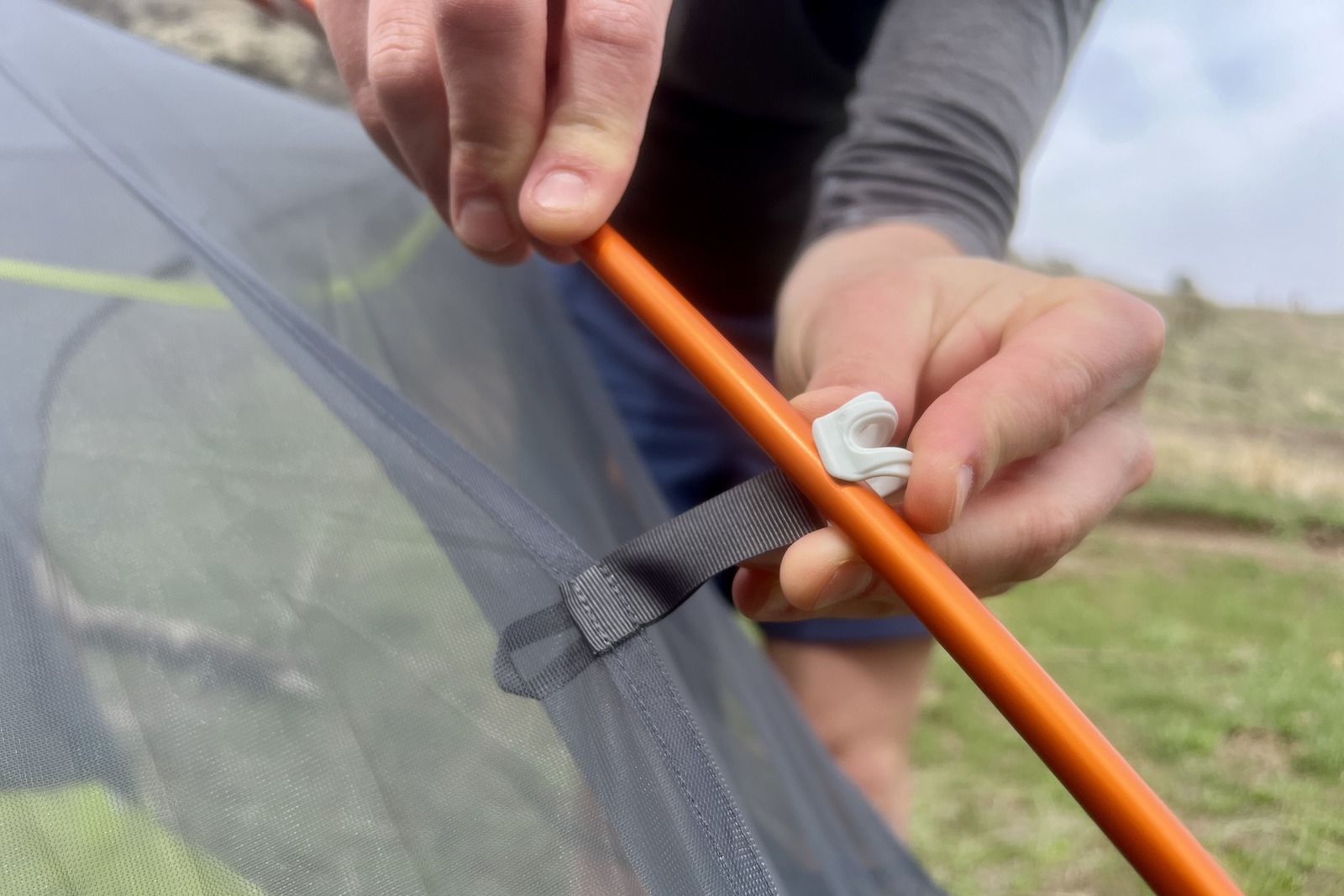 a close up of a hiker attaching a tent to its poles