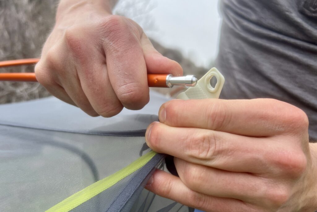 a close up of a hiker attaching a tent pole to a tent