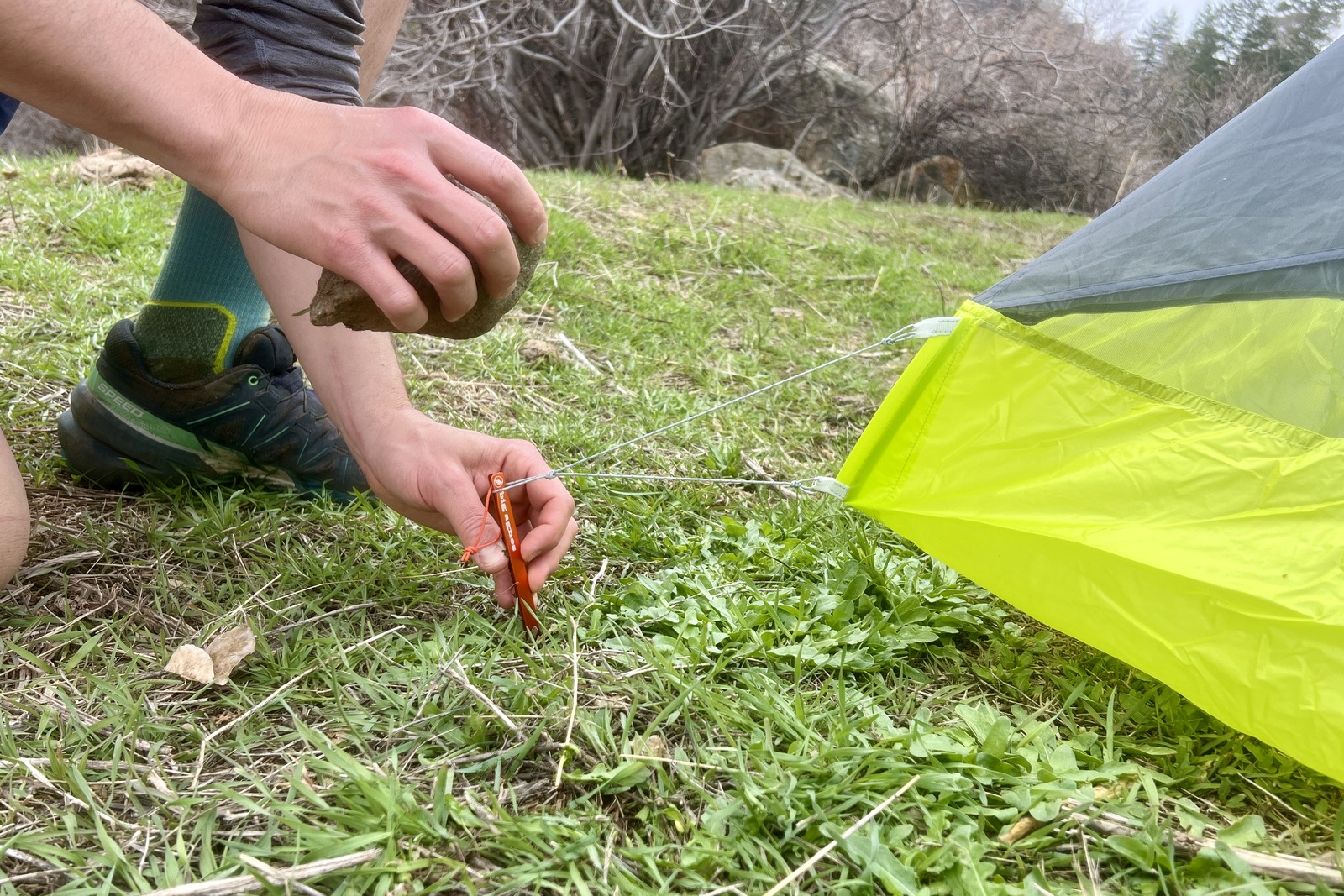 a close up of a hiker pounding in a tent stake with a rock