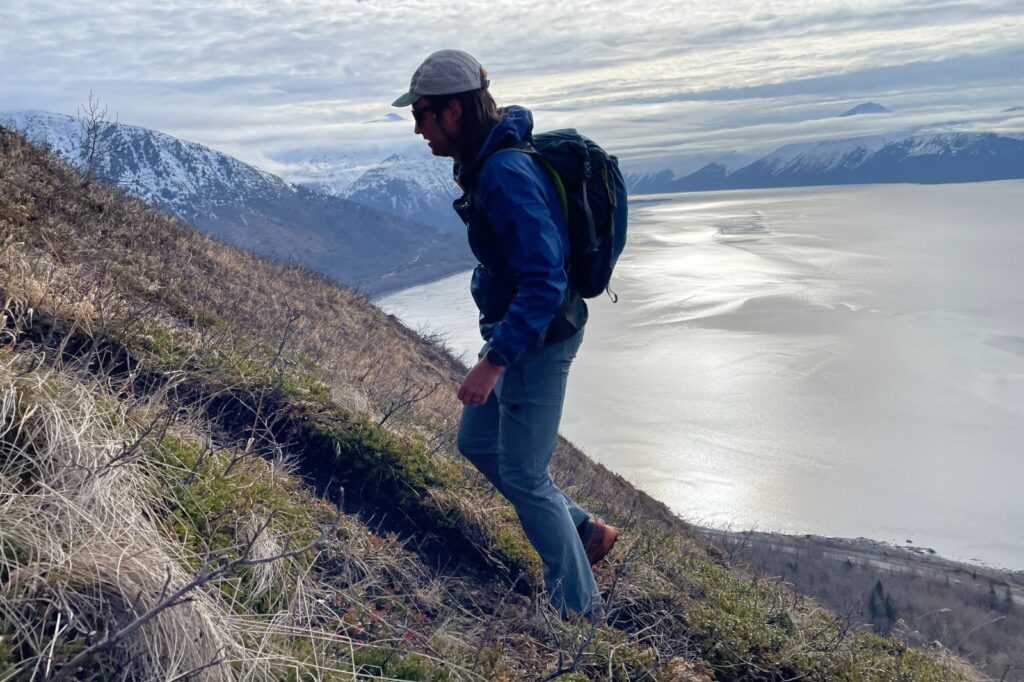A man hikes up a trail with mountains in the background.
