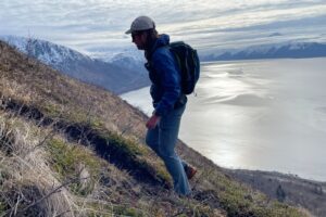 A man hikes up a trail with mountains in the background.