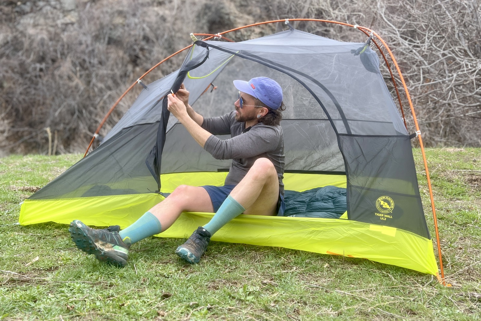 a hiker sits in a tent and ties back the door