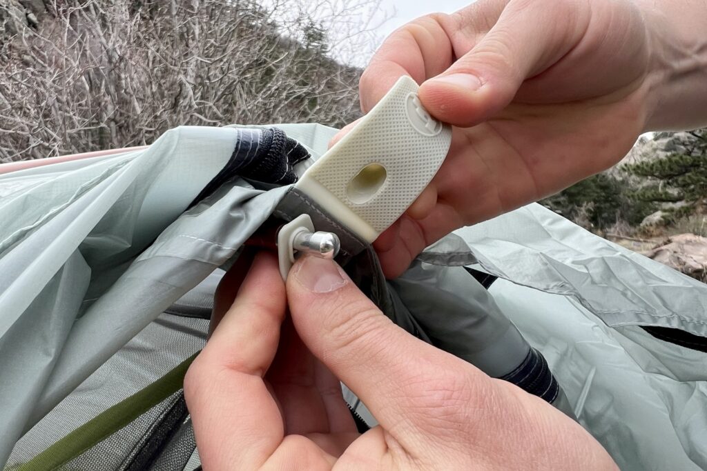 a close up of hands showing the rainfly connecton point on a tent