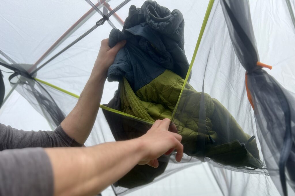 A hiker pulls a puffy jacket out of the gear loft in a tent