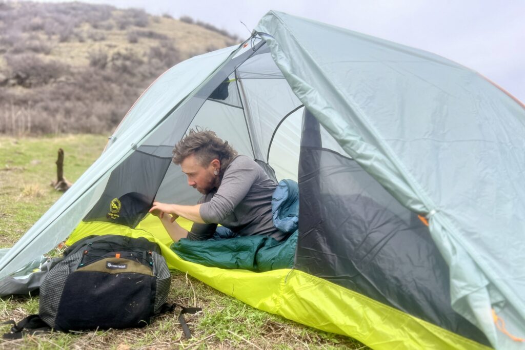 a hiker lays in a tent and sorts through the side pockets