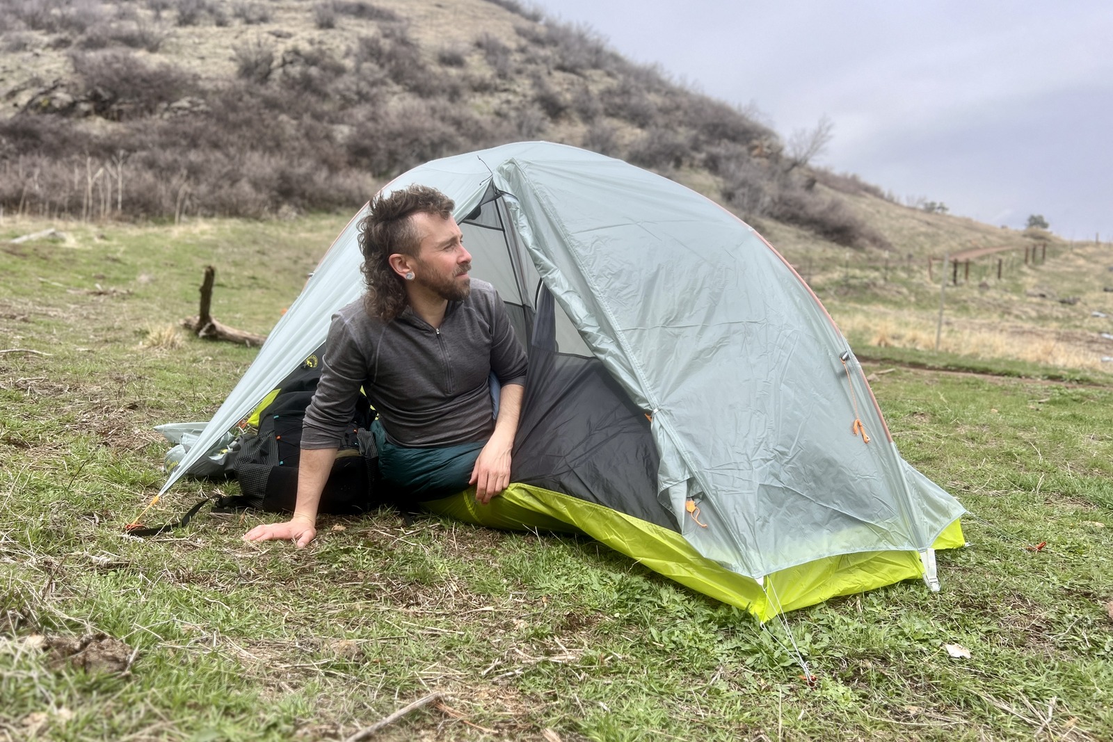 a hiker leans out of a light grey tent