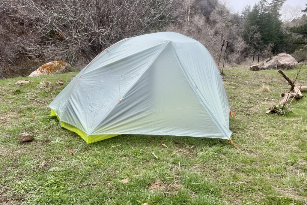 a green and light grey tent is pitched on some grass