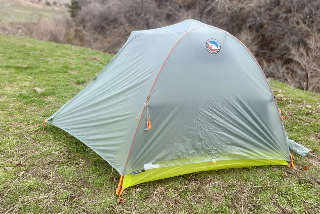 a green and light grey tent is pitched on some grass