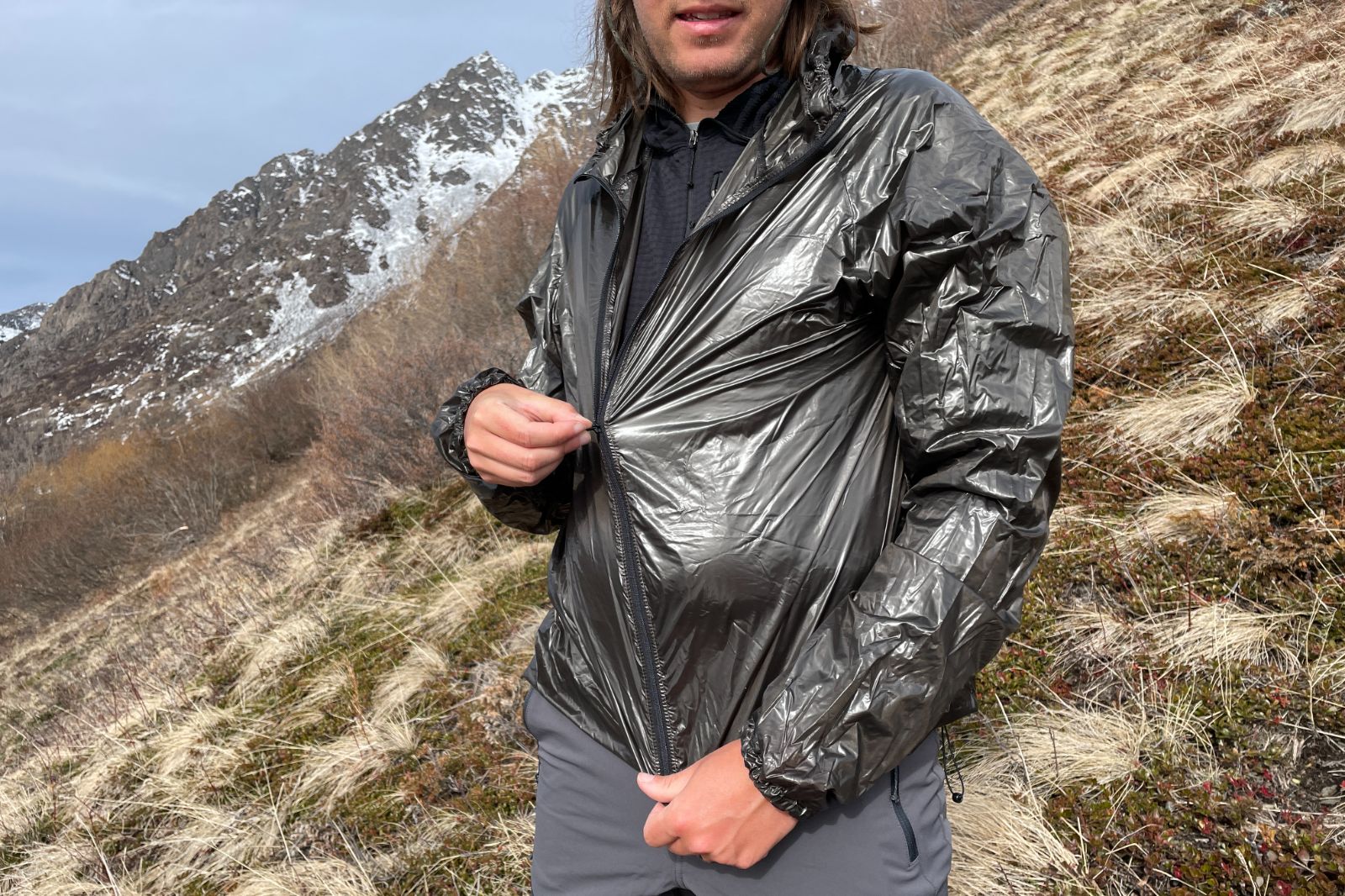 A man zips up a black windbreaker while on a trail.