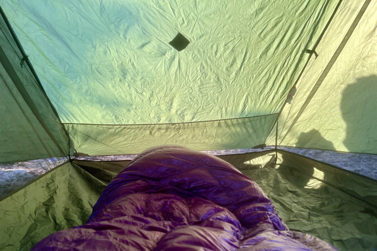 a POV view of a hiker in a purple sleeping bag sitting in a green tent