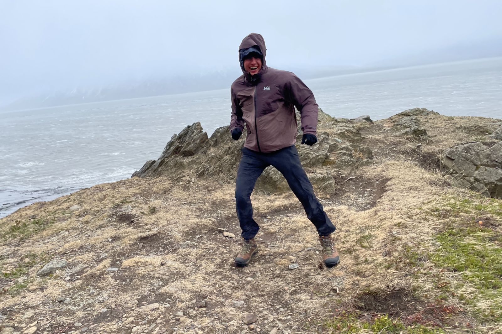 A man stands on a point above an ocean and mountain background.