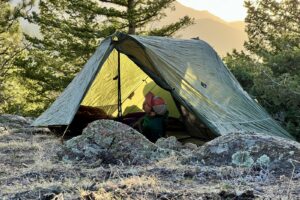 a hiker lounges in a green trekking pole tent at sunset