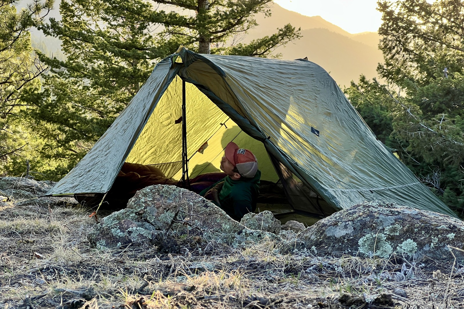 a hiker lounges in a green trekking pole tent at sunset
