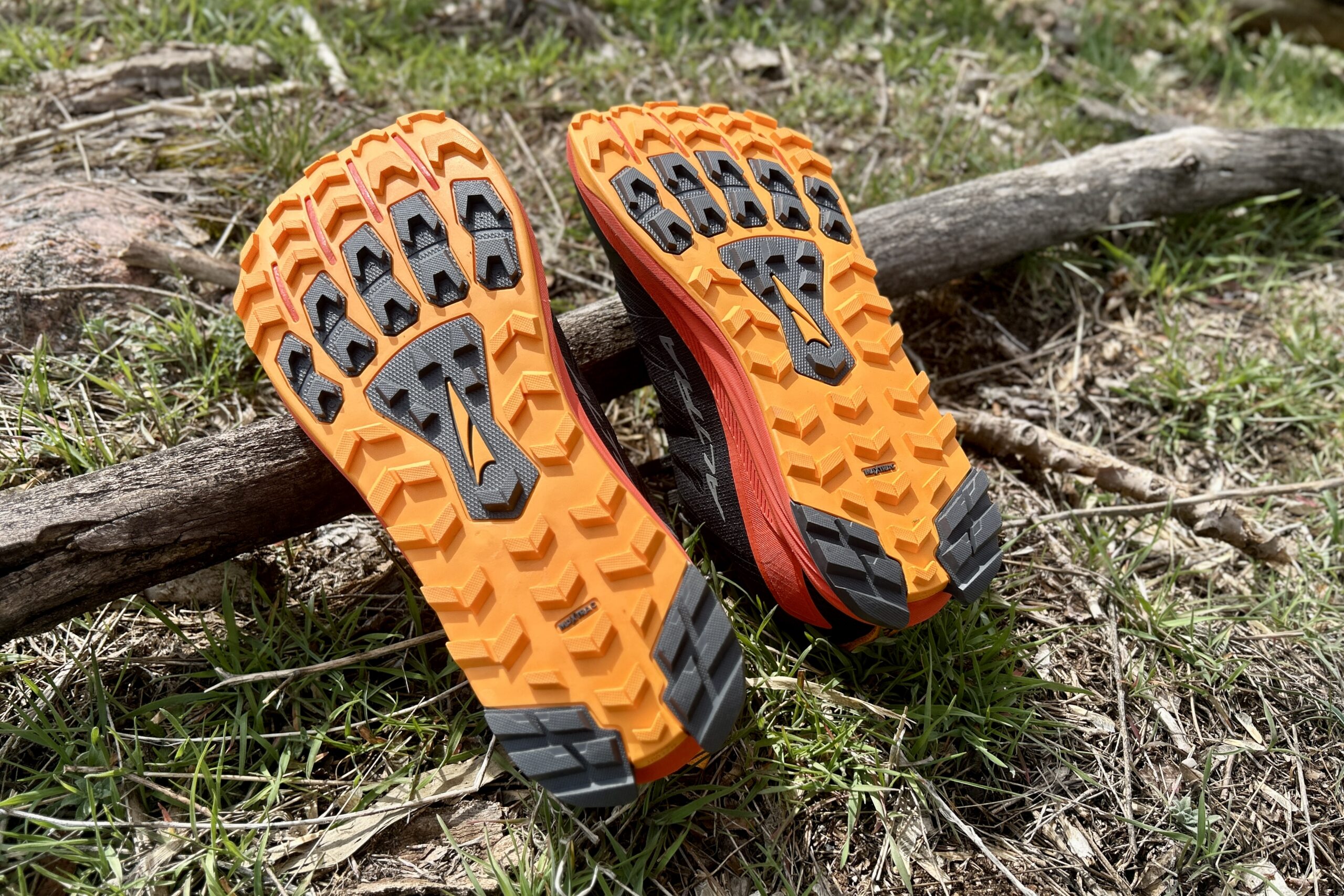 A pair of shoes lay upside down on some grass in the sun so the tread pattern is visible.